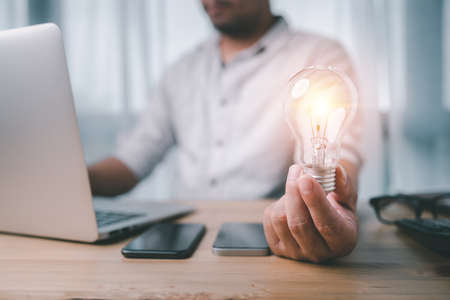 male hand holding a light bulb and he is using a notebook computer. The idea of ââinspiration from online technology. innovation idea concept.の写真素材