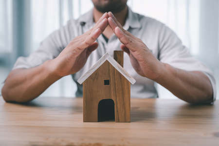 Property insurance and security concept. Protecting gesture of man and house model. Investment in real estate.の写真素材