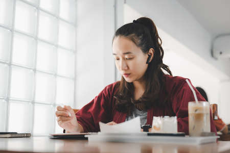 smart Asian woman copywriter working freelance project in modern cafe. Businesswoman using...