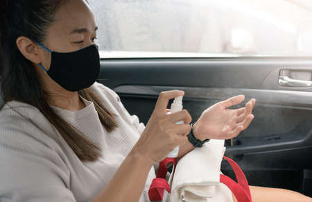 young Asian woman wears a black mask and sprays her hands with alcohol to prevent the COVID-19 or coronavirus in a taxi.の写真素材