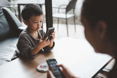 Daytime with family at home. baby cute boy playing games on a tablet or smartphone and watching cartoons. Mother working from home, using smartphone.の写真素材