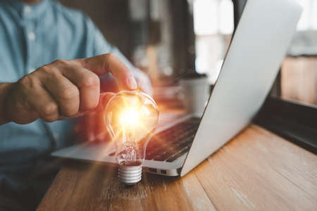 hand of a man with a lightbulb And he is using a notebook computer. The idea of ââinspiration from online technology. innovation idea concept.の写真素材