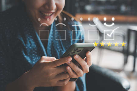 Customer service evaluation concept. smiling Asian female Is using a smartphone And she is smiling in satisfaction. Give five starの写真素材