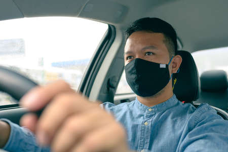 Asian man wears a black cloth mask. driving to pick up passengers. concept of coronavirus or COVID-19 protection on the taxi.の写真素材