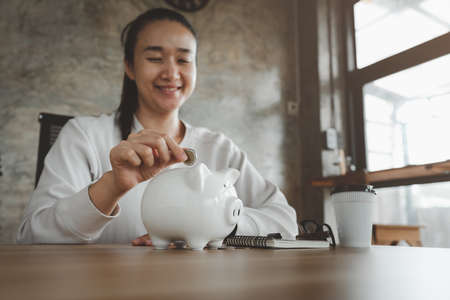 Happy smart asian woman saving money in a piggybank. saving and money concept.の写真素材