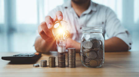 saving energy and money concept. idea for save or investment. businessman touch lightbulb on coins stacking on desk with calculator.の写真素材