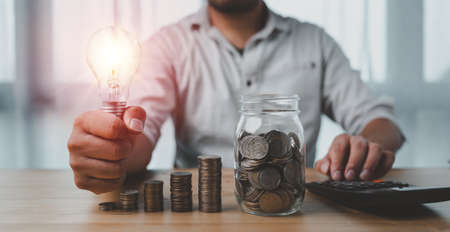 saving energy and money concept. idea for save or investment. businessman holding lightbulb on coins stacking on desk with calculator.の写真素材