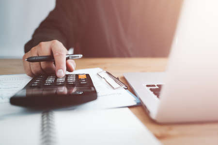bookkeeper using calculator counting finances taxes fees accounting calculate bills money planning budget loan payment concept pay online on computer do paperwork work at home office deskの写真素材