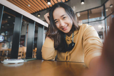 Young Asian teenager woman take Selfie at cafe, female using smartphone making vlog video to social...
