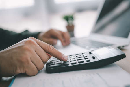 bookkeeper using calculator counting finances taxes fees accounting calculate bills money planning budget loan payment concept pay online on computer do paperwork work at home office deskの写真素材