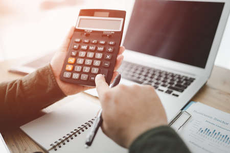 bookkeeper using calculator counting finances taxes fees accounting calculate bills money planning budget loan payment concept pay online on computer do paperwork work at home office deskの写真素材