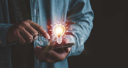 Businessman touching smartphone with light bulbs on the phone screen. ideas of new ideas with innovative technology and creativity.の写真素材