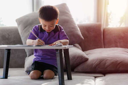 Asian Boy Doing homework with the intention. Child boy holding pencil writing, A boy drawing on white paper at the table, Elementary school and home schooling, Distance Education concept.の写真素材