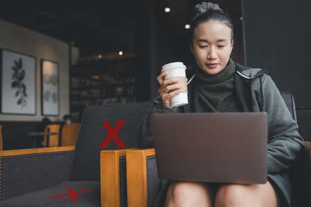 Asian girl sitting drinking coffee and use laptop, Social distancing rules in practice, alternate...