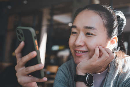 Happy Asian woman holding and using mobile phone in cafe or coffee shop with copy space.の写真素材
