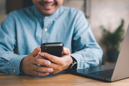 Entrepreneur Sitting at His Desk Works, Using Smartphone, Uses Social Media App, Emailing Business...