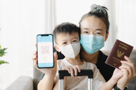 Asian mother and son wearing a face mask, is holding a passport and a smart phone with an example of a certificate of vaccination against the Covid-19 disease, new normal travel tourist concept.の写真素材