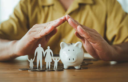 Businessman take a position to protect on the piggybank and paper family in hand, donation, saving,...