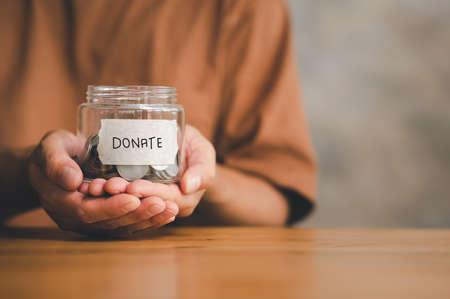 Man holding money jar with DONATE word written text label for giving and donation concept, saving,...