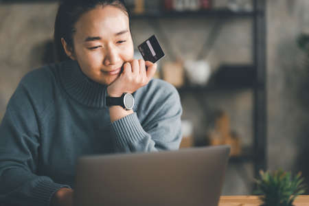 Happy Asian woman making online payment using laptop for shopping at home, technology online with...