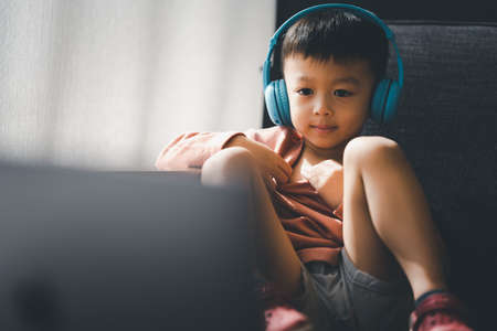 Asian boy watching and listening with laptop at home, using application online virtual class , social distancing, homeschooling, learning remotely during covid-19 coronavirus pandemic.の写真素材