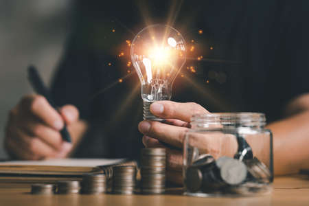 businessman holding lightbulb with using calculator to calculate and money stack. idea saving energy and accounting finance in home office concept, Business, finance, investment, Financial planning.の写真素材