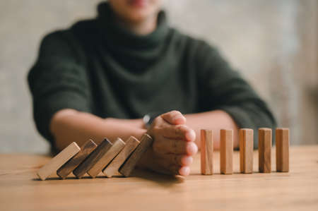 Hand Stopping the domino business crisis effect or risk protection concept, business solution and intervention.の写真素材