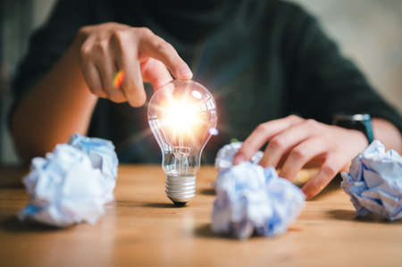 new idea and light bulbs concept with woman hand touching light bulb and crumpled office paper, businesswoman show new ideas with innovative technology and creativity.の写真素材