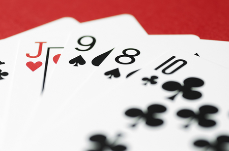 Playing cards are laid out like a fan. Red background, close up, soft focus