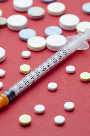 Insulin syringe in the center and round pill, red backgroundの写真素材