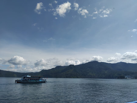Distant boat sailing on lake with rolling hills along shoreline beneath bright clear blue skyの写真素材