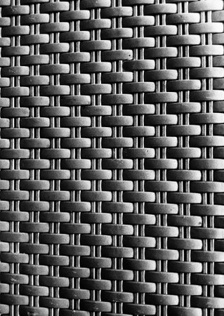 Monochrome close up of woven synthetic rattan texture forming repeating geometric pattern background