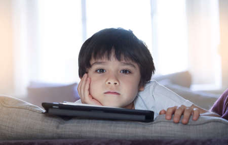 High key portrait Kid stay at home relaxing in living room in sunny day summer, Happy child boy lying on sofa watching cartoon or playing game,Home schooling,Social Distance, E-learning online educationの写真素材