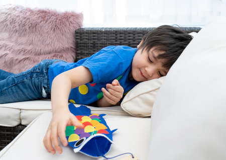 High key happy kid stay at home lying on sofa playing with Koinobori (Carp streamers),Child boy doing Japanese fish kite in sunny day summer, Distance education or Home schooling, Children's Dayの写真素材