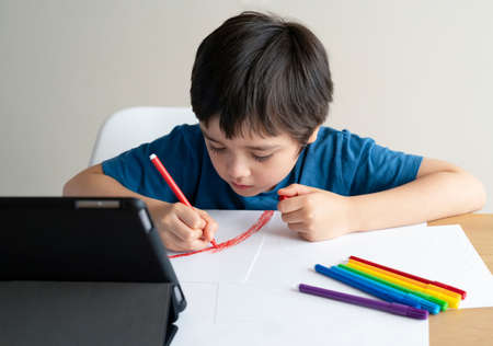 Kid coloring his own rainbow drawing on paper,Child using digital tablet searching information on...