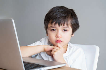 Portraitschool kid crying after internet log off, Sad boywith sad face watching cartoon on laptop,Bored Child looking at camera with upset face,Social Distancing,E- learning online educationの写真素材