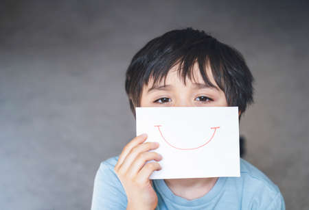 Portrait of bored kid with sad face holding  white paper with smile, Child boy getting bore stay at home during during self-isolation, quarantine. Coronavirus outbreak and flu covid epidemicの写真素材