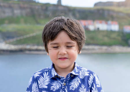 Head shot boy face with eyes closed standing alone by the sea, Happy kid laughing while closing his eyes, Candid shot Child playing hide-and-seek  in the beach, Positive children conceptの写真素材