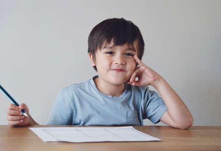 Portrait of preschool kid boy making homework at home. Happy Child holding pencils and looking at...