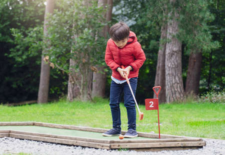 Portrait of Happy child playing mini golf in the park, Active Kid boy playing crazy golf on holiday, Children enjoying his vacation outdoors activityの写真素材
