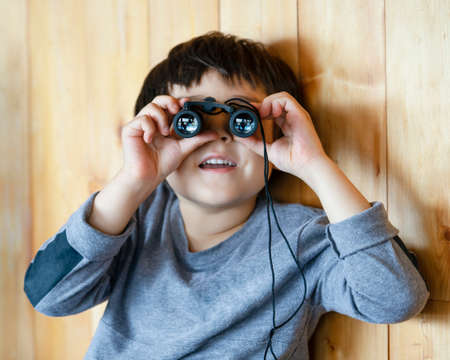 Portrait cute little boy looking through of binoculars in the animals station view point, Child explorer and learning about wild nature in countryside.Summer campの写真素材