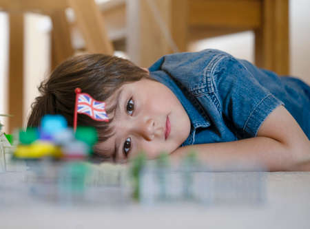 Selective focus of little boy lying on floor looking out deep in through, Positive child laying on carpet relaxing and playing with soldiers and figurine toy, Cropped shot kid looking at his plastic toysの写真素材