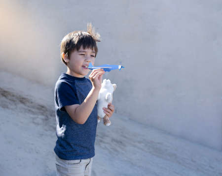Portrait happy boy playing with toy airplane against blurry wall background, Child throwing foam airplane, Kid playing outside in the summer,  Childhood outdoor activity concept.の写真素材