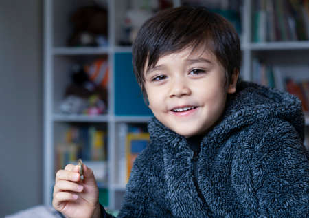 Portrait of little kid holding one pound coins and looking at camera with smiling face, Happy boy showing his money on his hand for school, donation or saving for the futureの写真素材