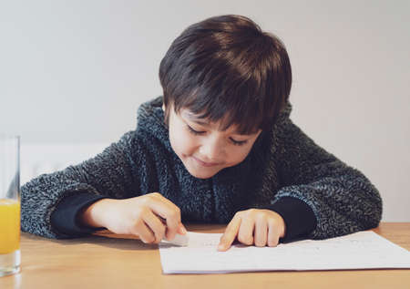 Portrait of adorable kid doing  homework with happy face, Female cute child boy using rubber rubbing...