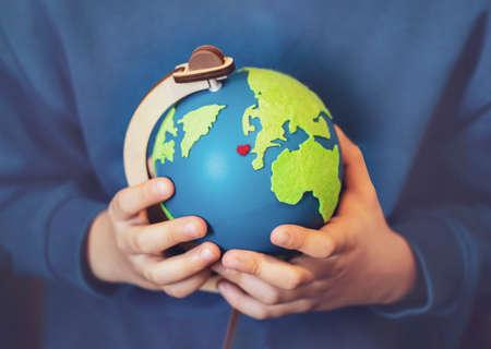 Cropped shot little boy holding the earth in his hands. Hands holding globe with red heart on map,...