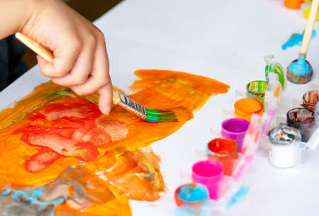 Selective focus Children's hand painting on white paper with water color, Cropped shot of kid holding brush paint, Hand painting bright colour of orange and red on the paper.の写真素材