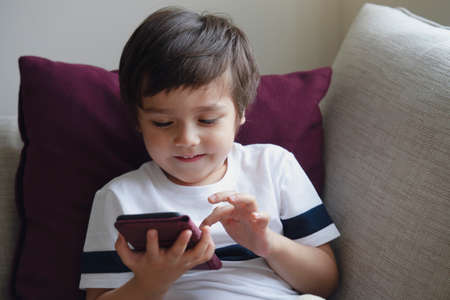 Happy little boy having fun playing game on mobile phone,Preschool kid sititng on sofa with smiling...