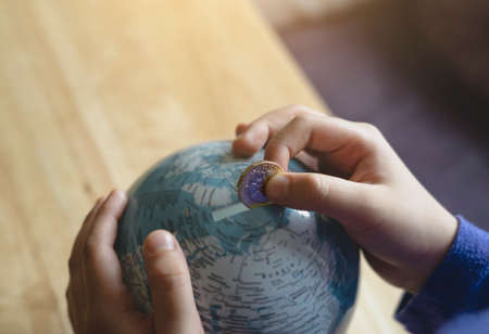 Kid hand putting one pound coin into piggy bank to donate money helping the earth, Hand holding...