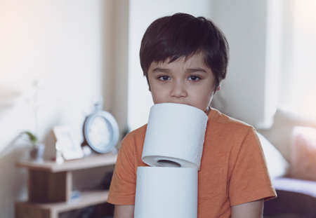 Child carrying a stack of toilet paper with blurry living room background, kid holding toilet roll,...